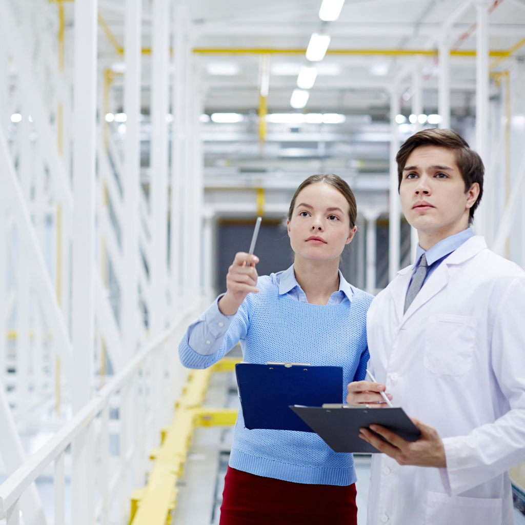 Mulher e homem conversando em ambiente industrial utilizando softwares de controle pelo notebook e tablet.