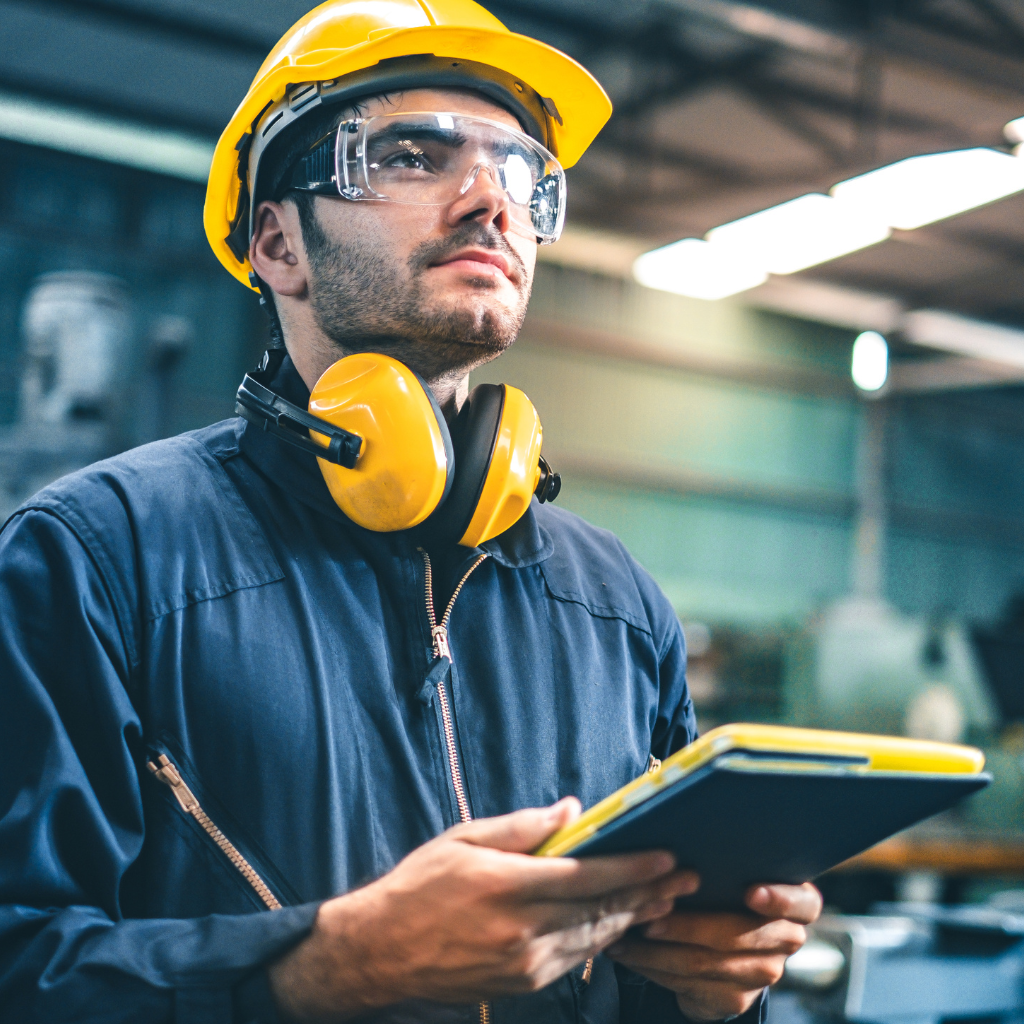 Homem em ambiente industrial vestido com equipamentos de proteção e controlando a planta industrial pelo software no tablet.